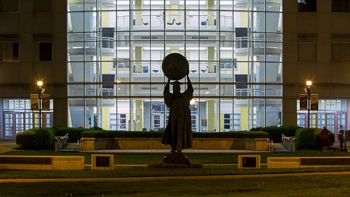 Evening view of Citizen Scholar statue backlit by Strong Hall.