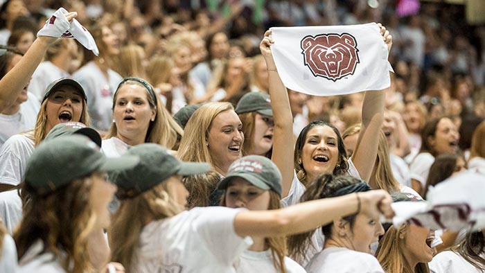 Student holding a Bear head flag among a large group of students.